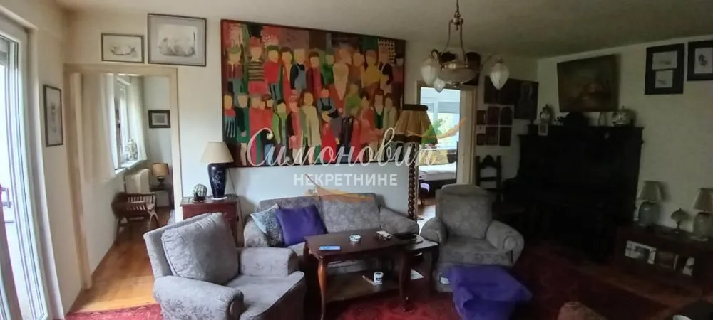 Dnevna soba sa garniturom, foteljama i velikom umetničkom slikom na zidu.