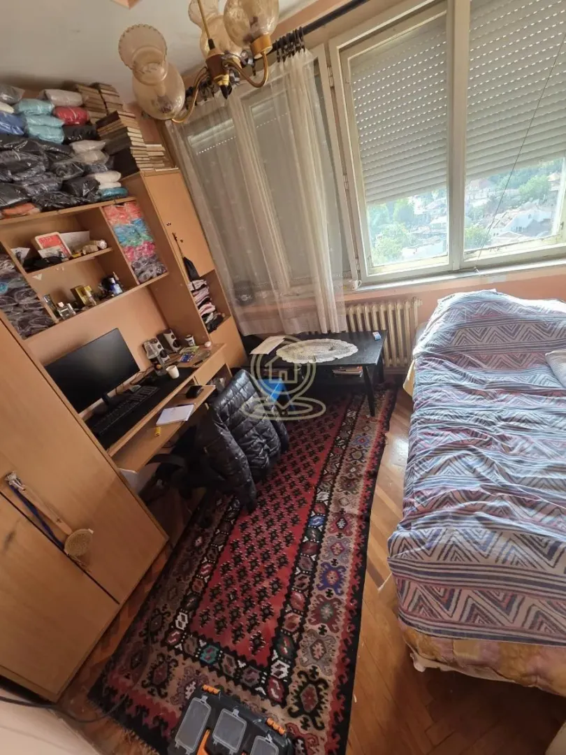 Nameštena spavaća soba sa krevetom, radnim stolom i velikim prozorom.