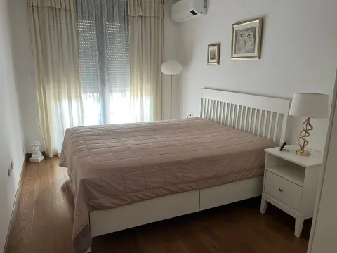 Svjetla spavaća soba sa bračnim krevetom, bijelim noćnim stočićem i prozorom sa zavjesama. - image 5