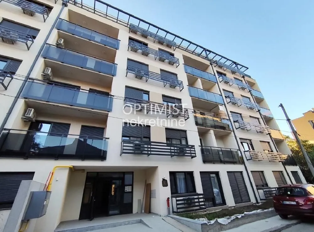 Pogled na spoljašnjost moderne stambene zgrade sa balkonom i ulazom.