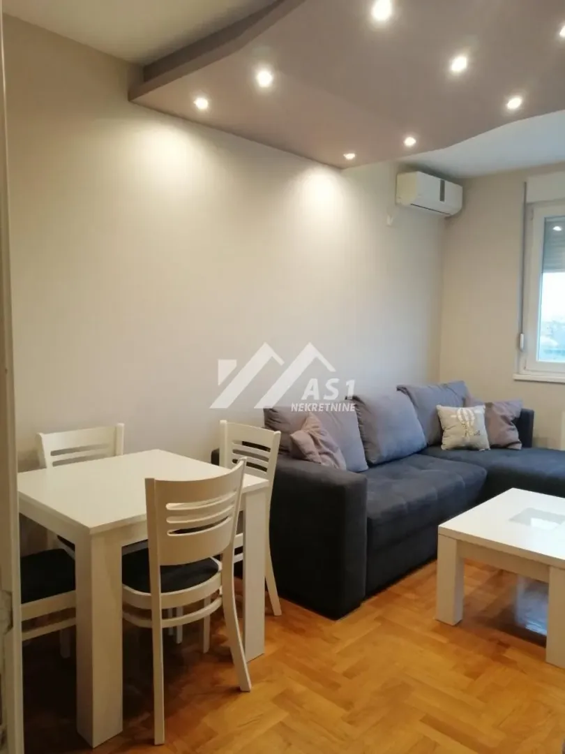 Dnevna soba sa garniturom, trpezarijskim stolom i parketom na podu.