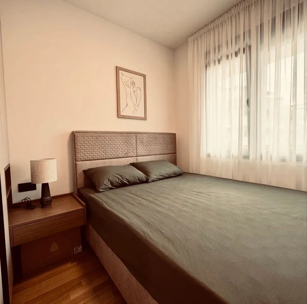 Udobna spavaća soba sa bračnim krevetom, noćnim stočićem i prozorom prekrivenim zavjesama.