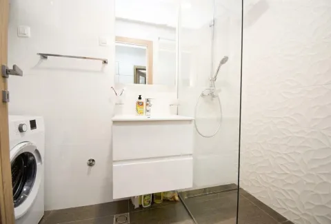 Modern bathroom with a sink, shower cabin, and washing machine. - image 7