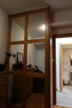Spavaća soba sa velikim drvenim ormanom sa ogledalima i pogledom na kupatilo. - image 2