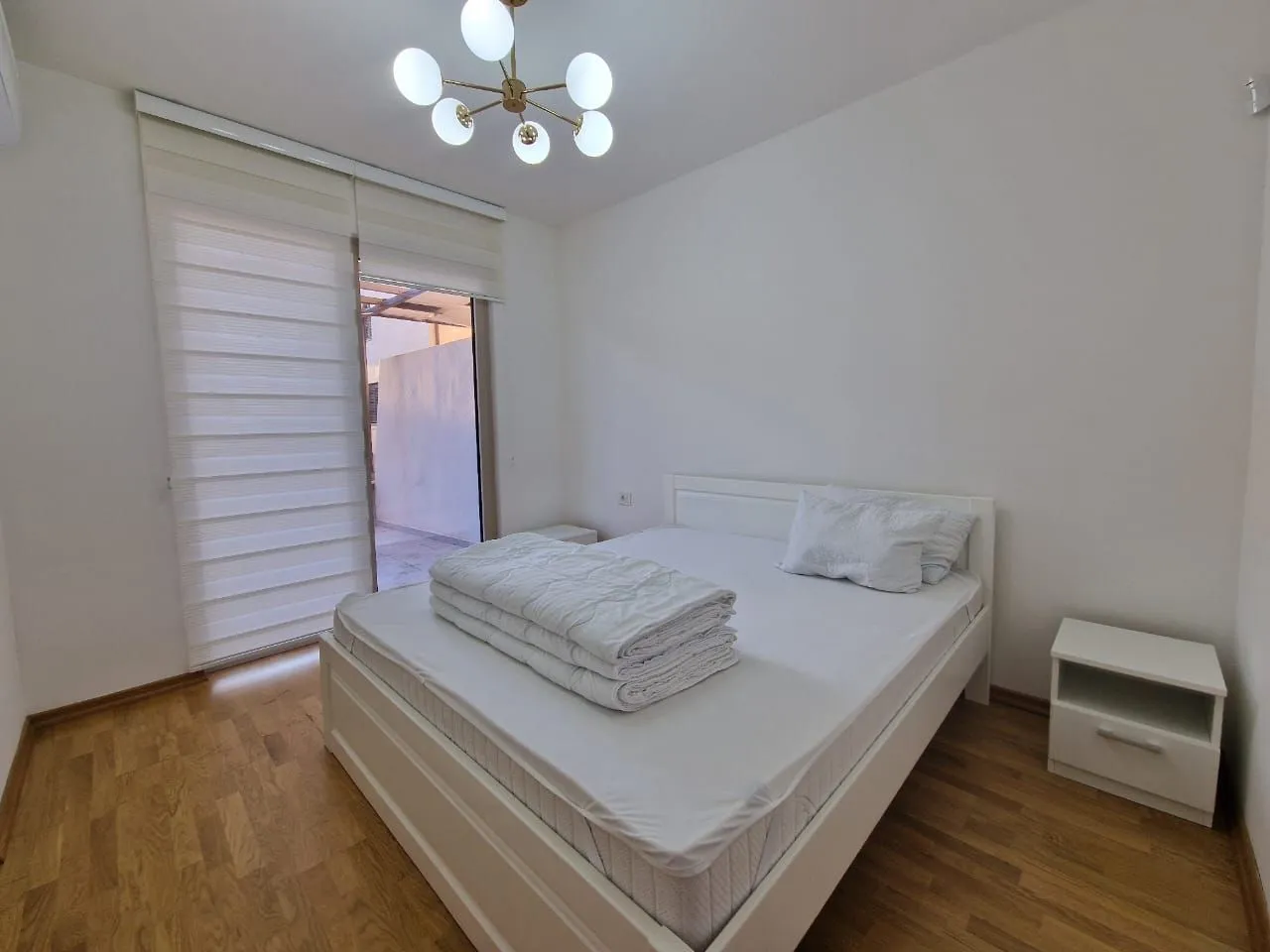 Bright bedroom with a white bed, bedside table, and access to the terrace.
