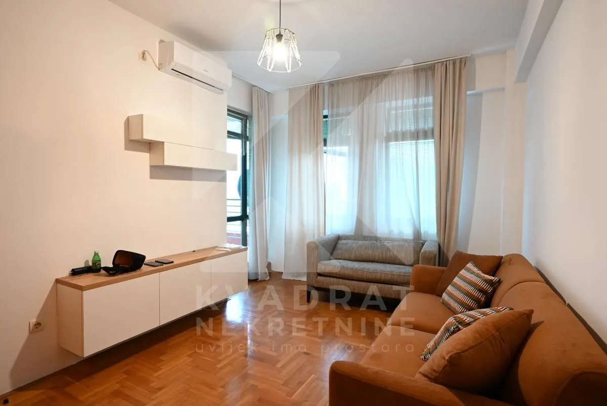 Living room with sofa, TV unit and hardwood flooring.