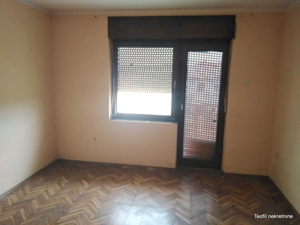 Prazna soba sa parketom na podu i izlazom na terasu.