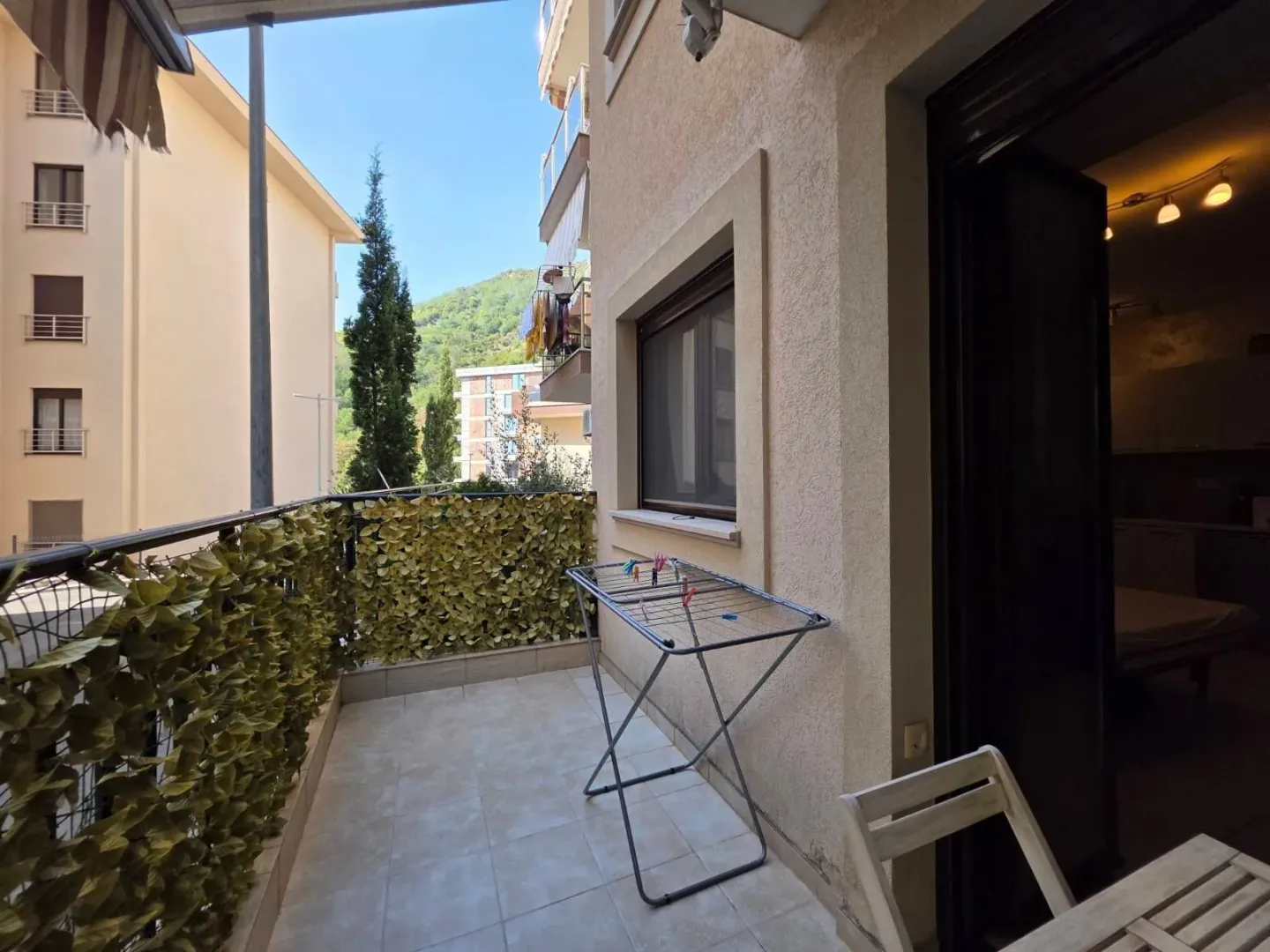 Natkriveni balkon sa stalkom za sušenje veša i pogledom na okolne zgrade i zelenilo.