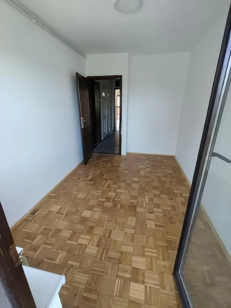 Prazna soba sa parketom i otvorenim vratima.