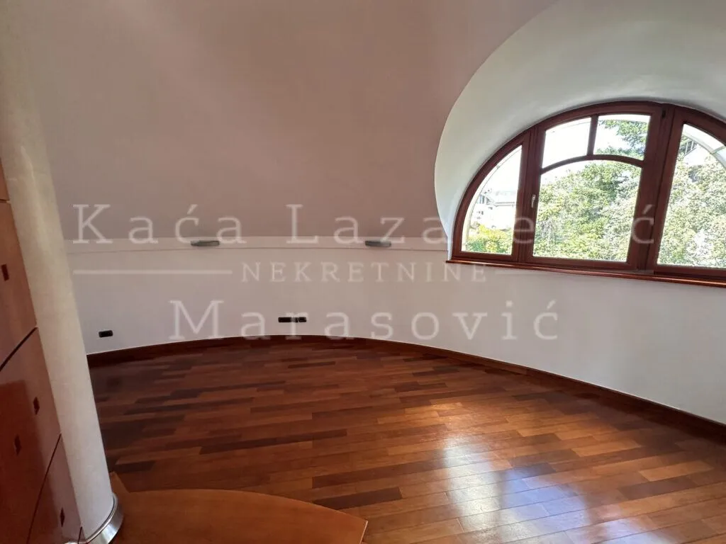 Prazna prostorija sa drvenim podom i velikim lučnim prozorom.