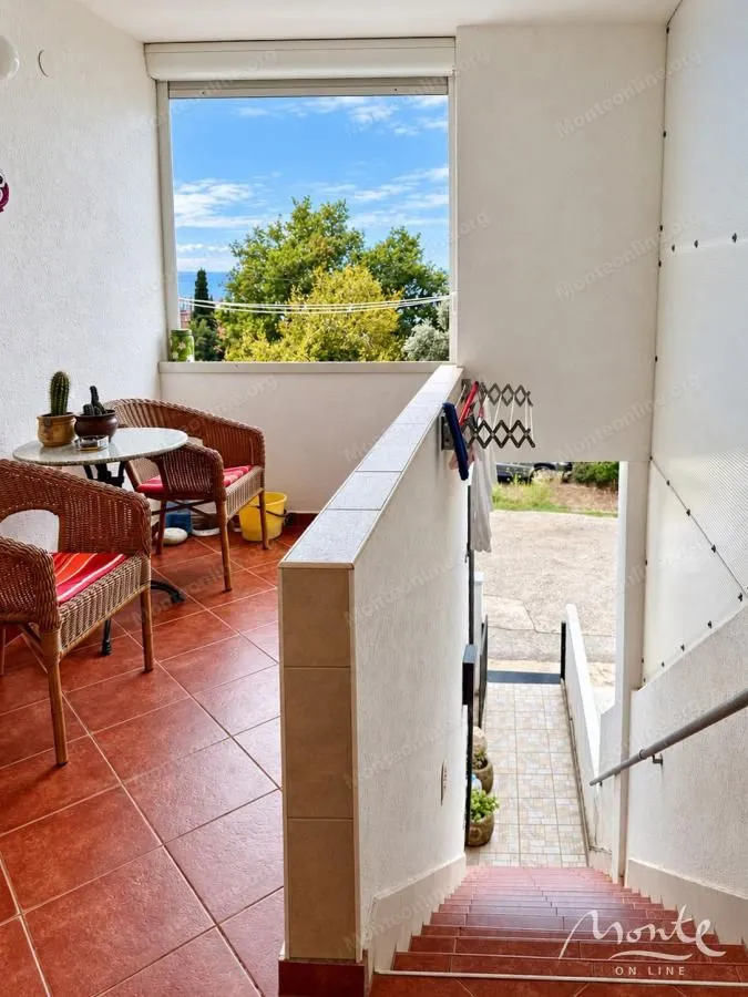 Natkriveni balkon sa garniturom za sjedenje i pogledom na zelenilo i more.