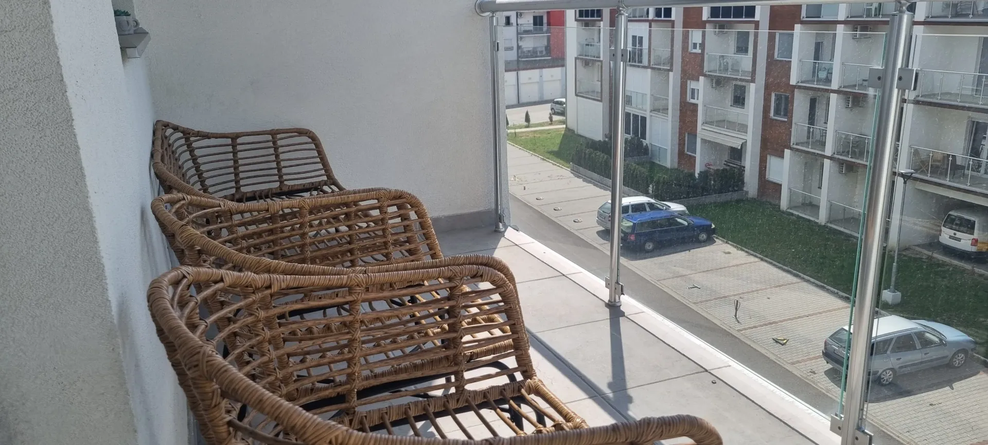 Manji namešteni balkon sa pogledom na parking i zgrade u okruženju.