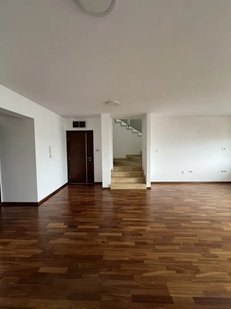 Spacious empty room with wooden flooring and stairs in the background.