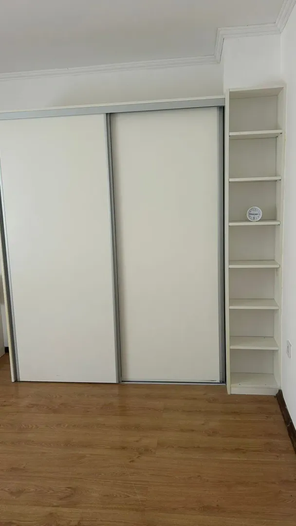 Bijeli ugradni garderober sa kliznim vratima i otvorenim policama u sobi.