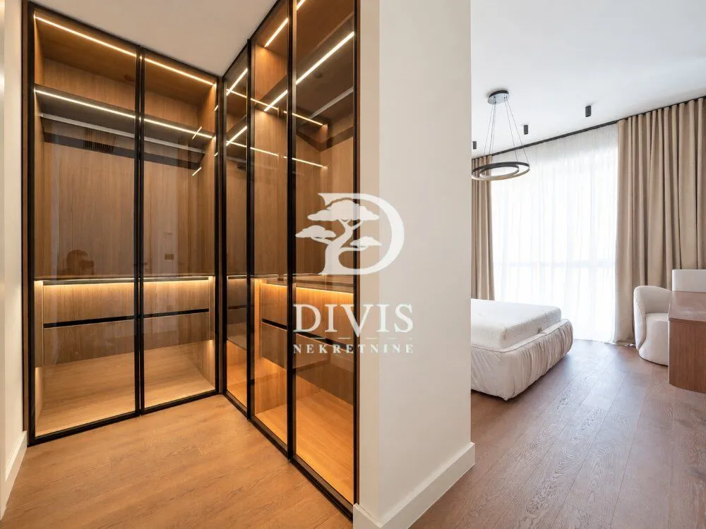 Modern walk-in wardrobe with glass doors and integrated lighting inside the bedroom.