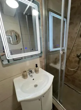 Modern bathroom with a sink, illuminated mirror, and walk-in shower. - image 7