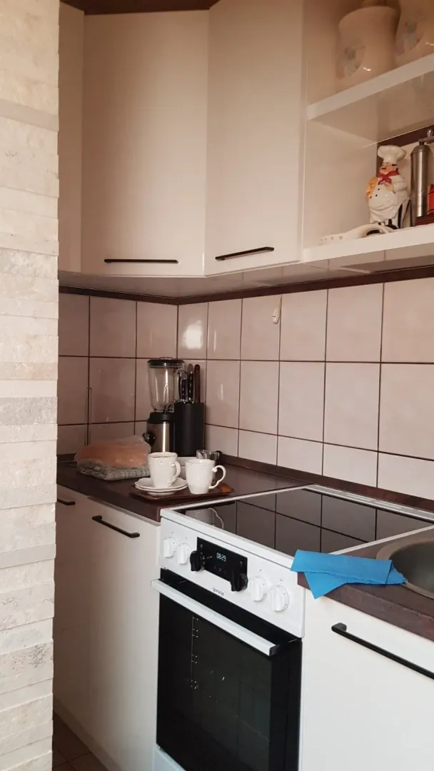 Mala funkcionalna kuhinja sa bijelim elementima i električnim šporetom.