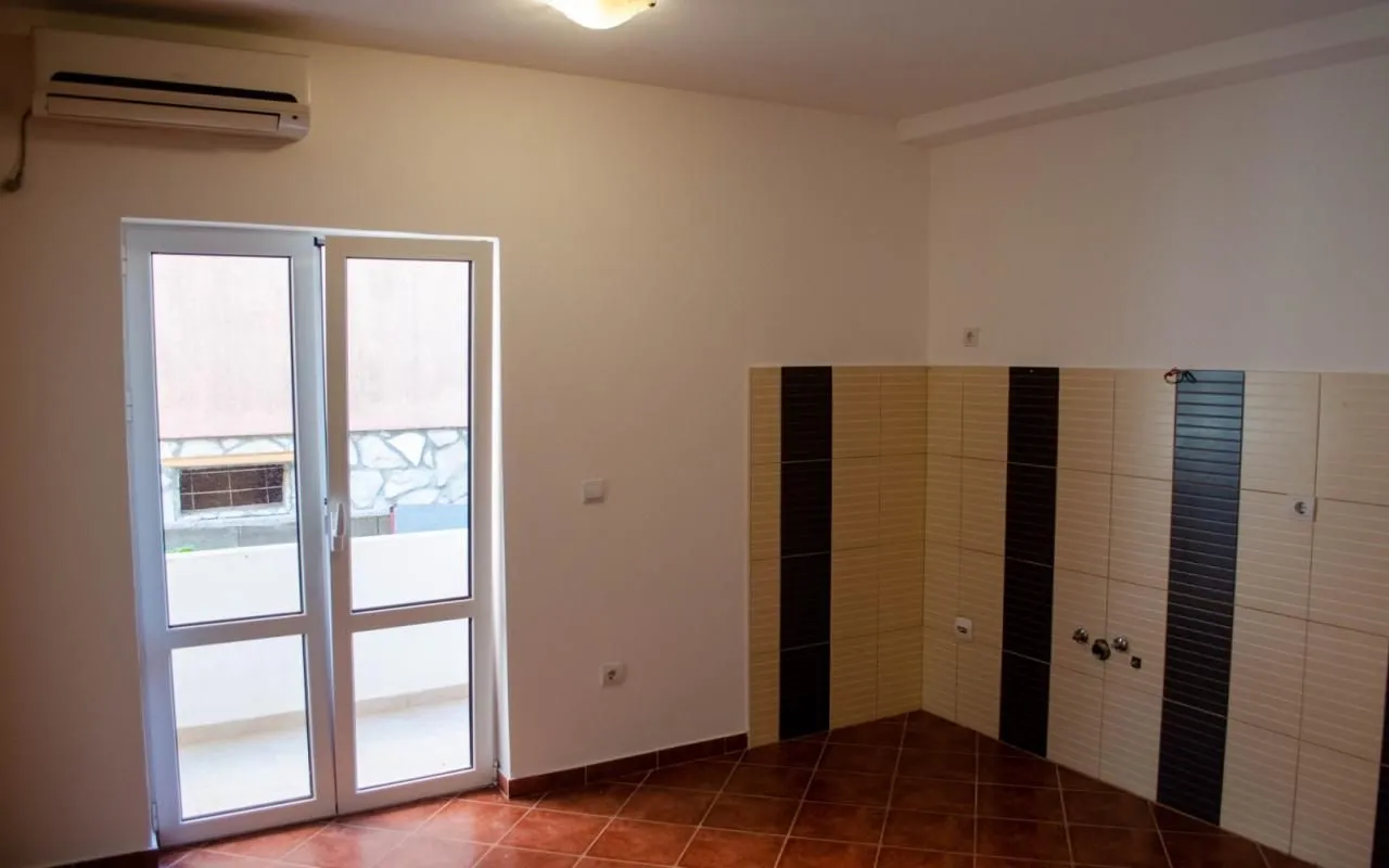 Manja kuhinja sa keramičkim pločicama, klima uređajem i balkonskim vratima.