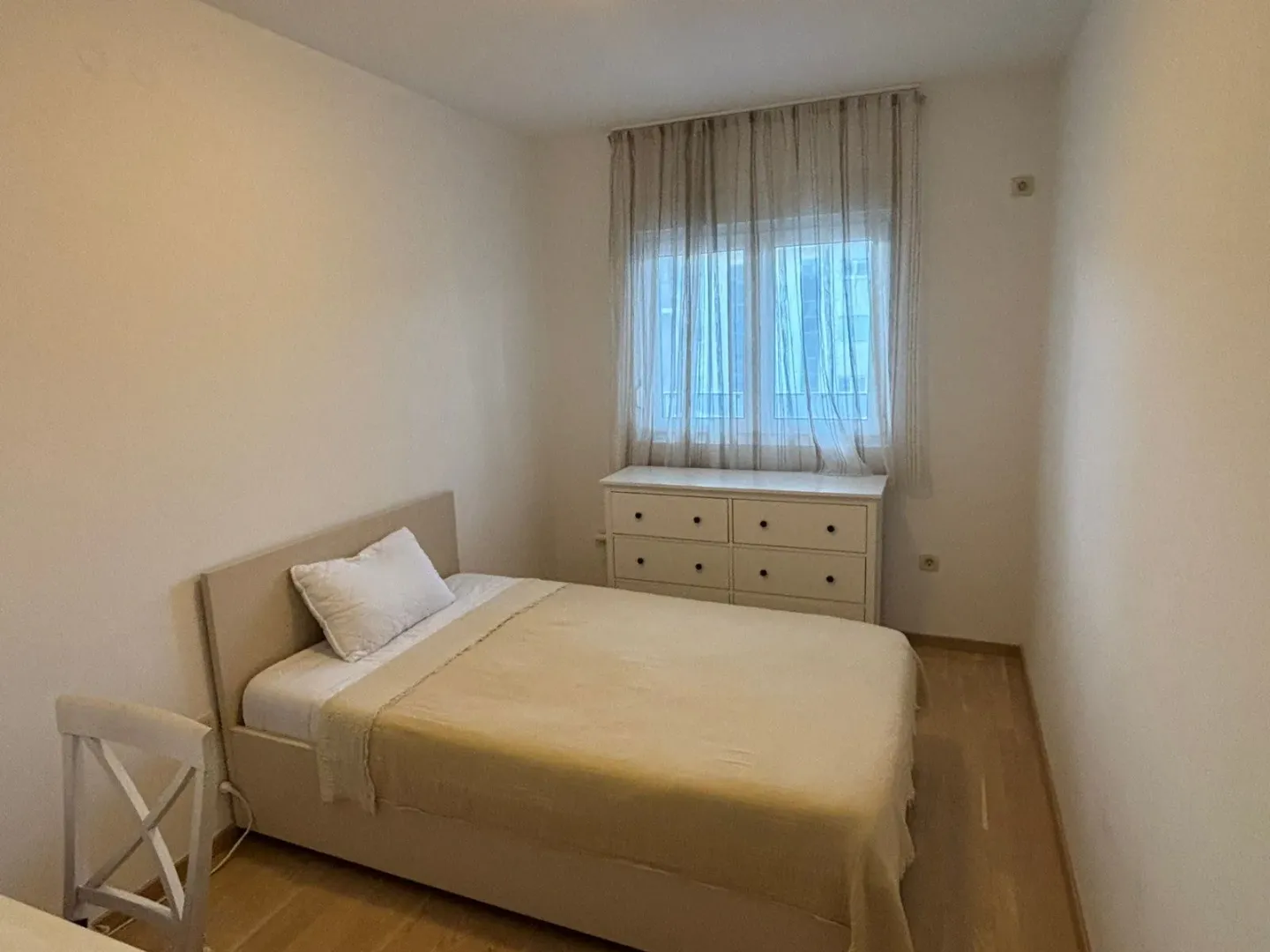 Furnished bedroom with a double bed, chest of drawers, and a window with curtains.