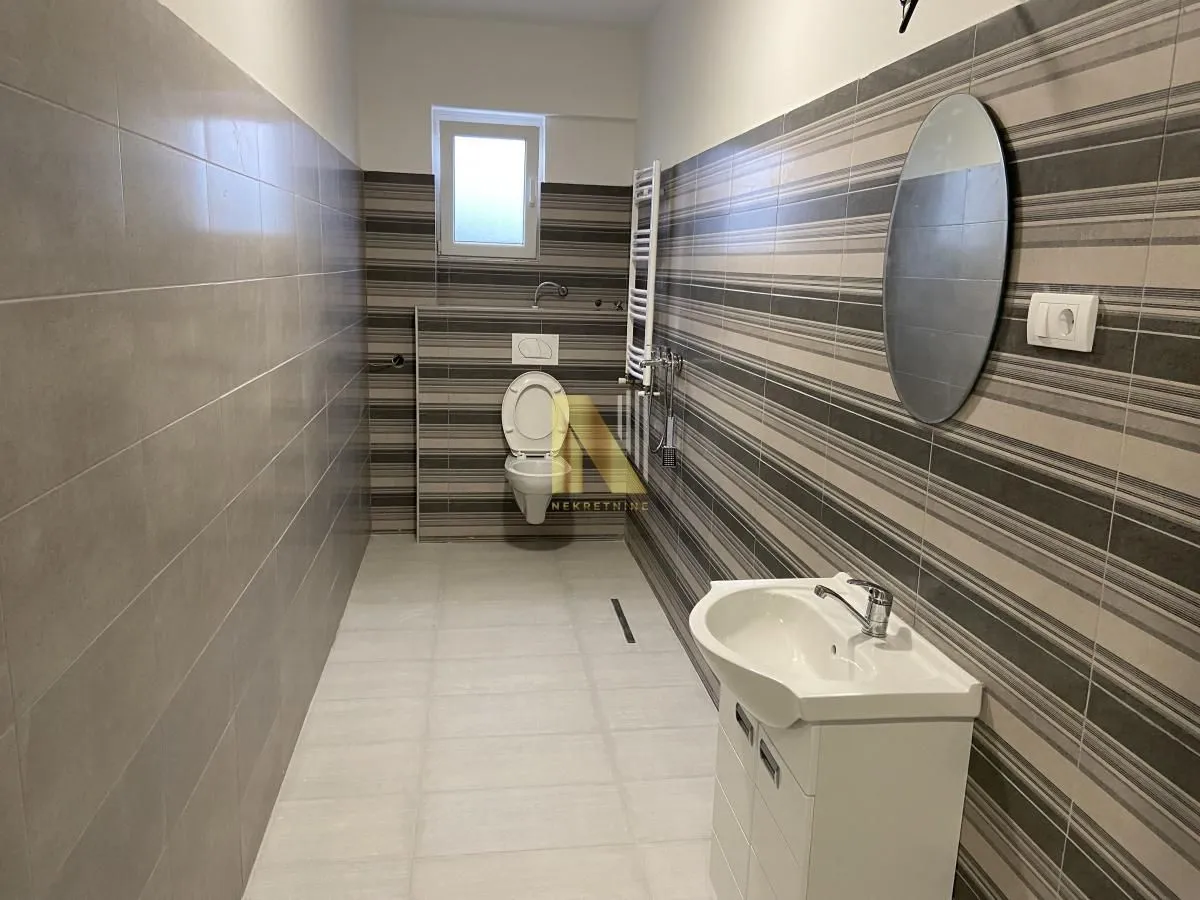 Long tiled bathroom with a sink and a toilet.