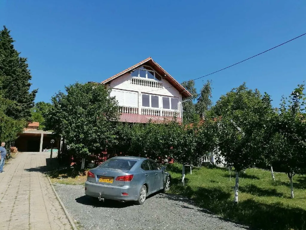 Eksterijer kuće sa dvorištem, voćnjakom i parkiranim automobilom.