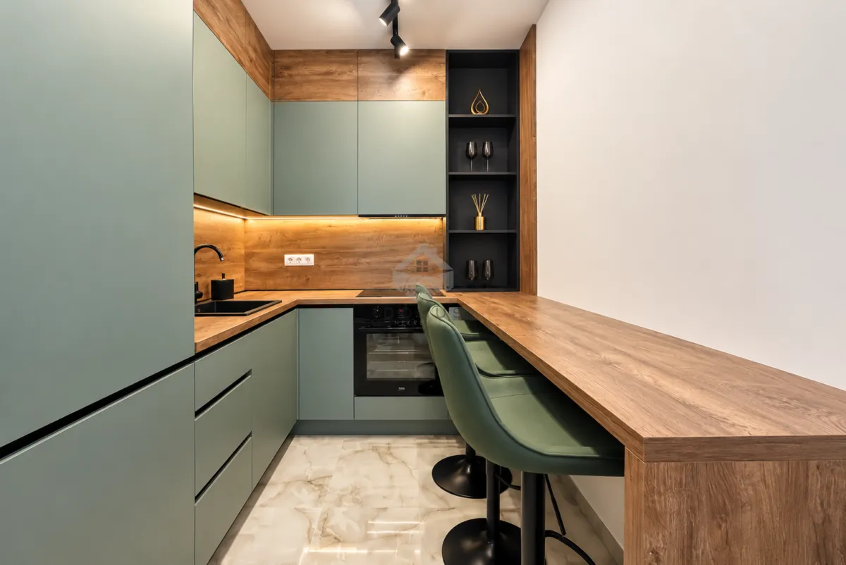 Modern kitchen with green cabinets, wooden details, and a breakfast bar with bar stools.