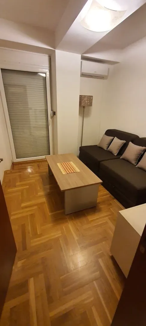 Manja dnevna soba sa garniturom i drvenim stolom.