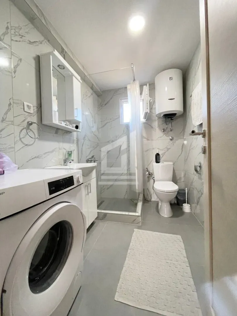 Modern bathroom with a shower cabin, sink, toilet, and washing machine.