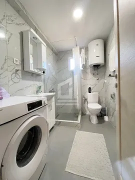 Modern bathroom with a shower cabin, sink, toilet, and washing machine. - image 10