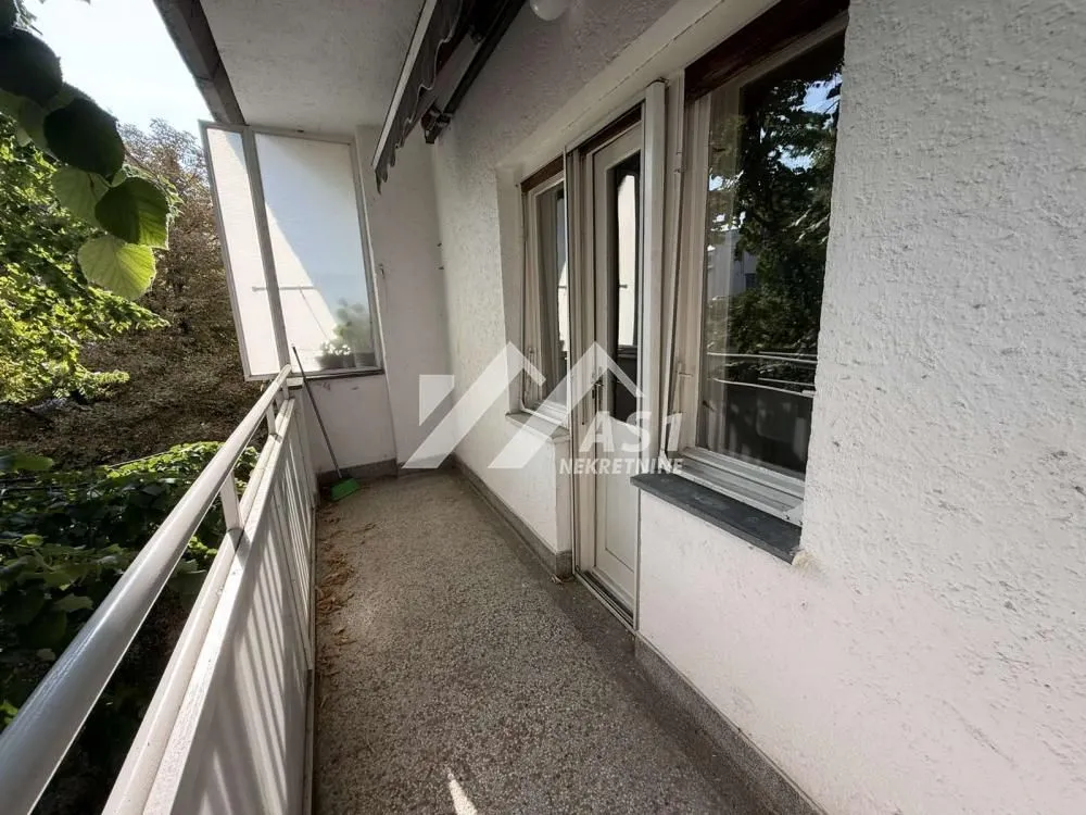 Dugi balkon sa metalnom ogradom i pogledom na zelenilo.