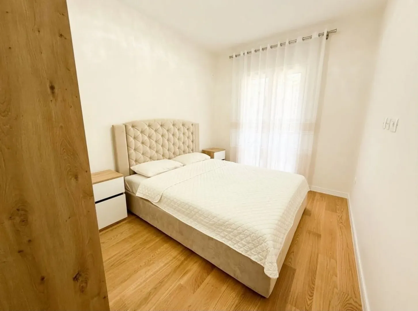 Bright bedroom with a double bed, bedside tables, and a window with curtains.