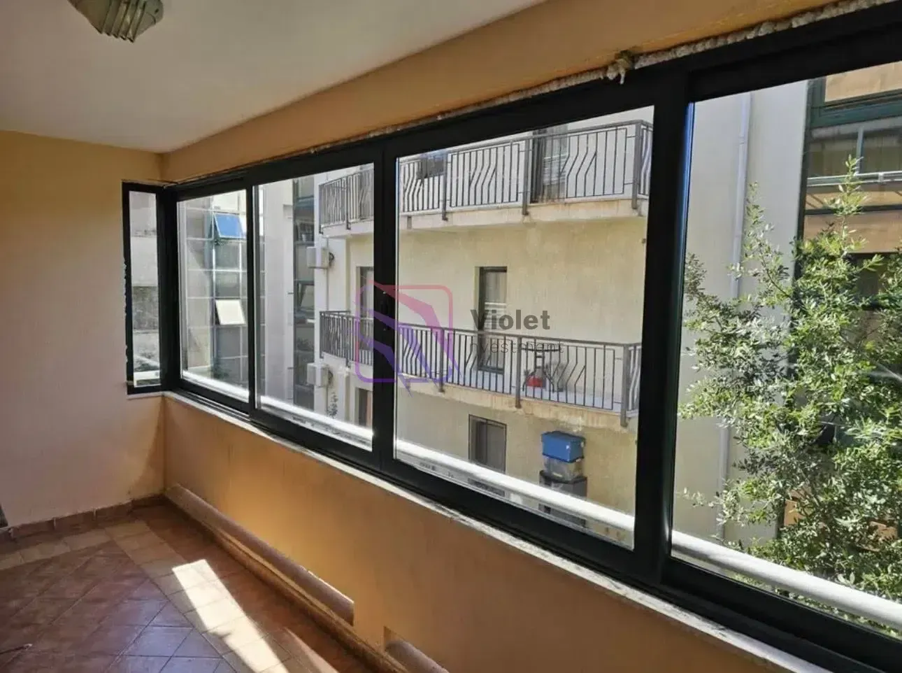 Zastakljeni balkon sa pogledom na susjedne zgrade.