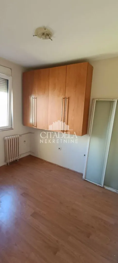 Prazna soba sa drvenim ormarom na zidu i laminatom na podu.