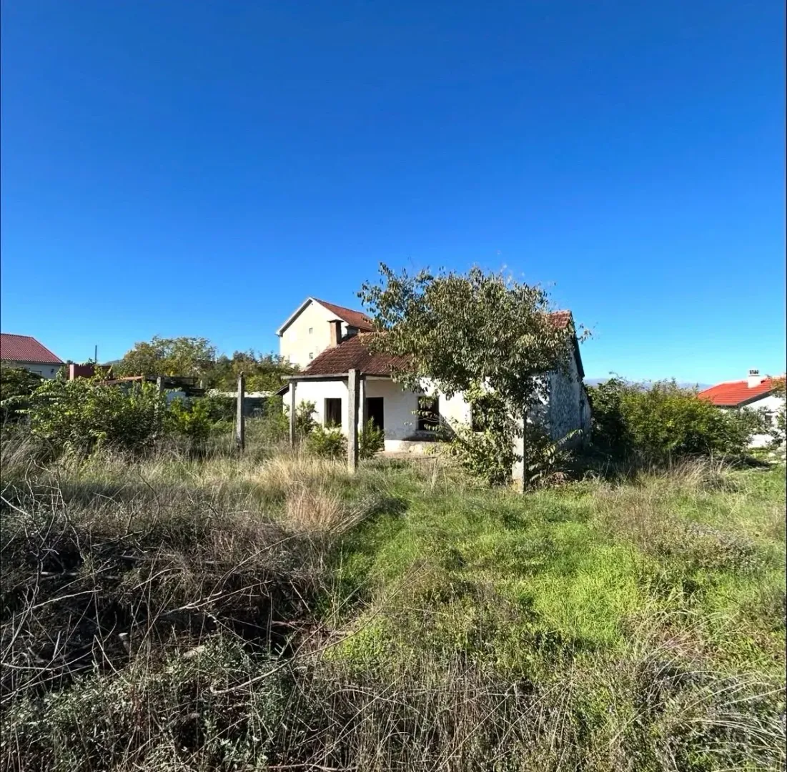 Pogled na stariju kuću sa dvorištem i zelenilom.