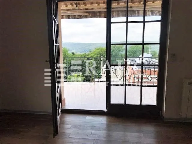 Pogled iz sobe na terasu i zeleni pejzaž kroz staklena balkonska vrata.