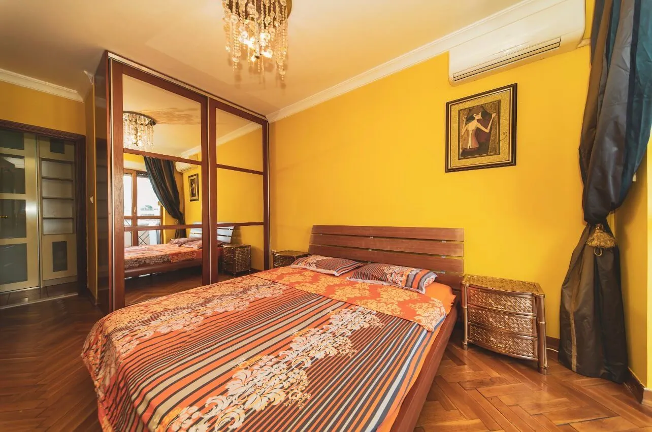Furnished bedroom with a double bed, large mirrored wardrobe, and yellow walls.