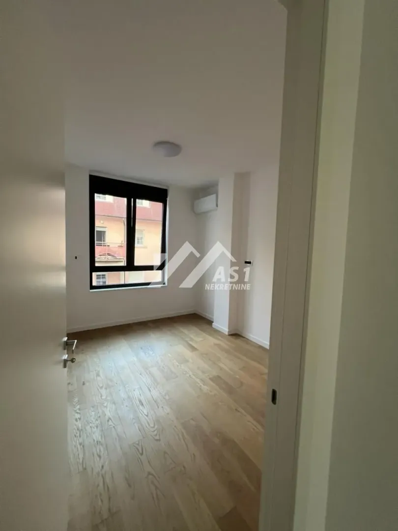 Empty room with wooden flooring and a window viewed through a doorway.