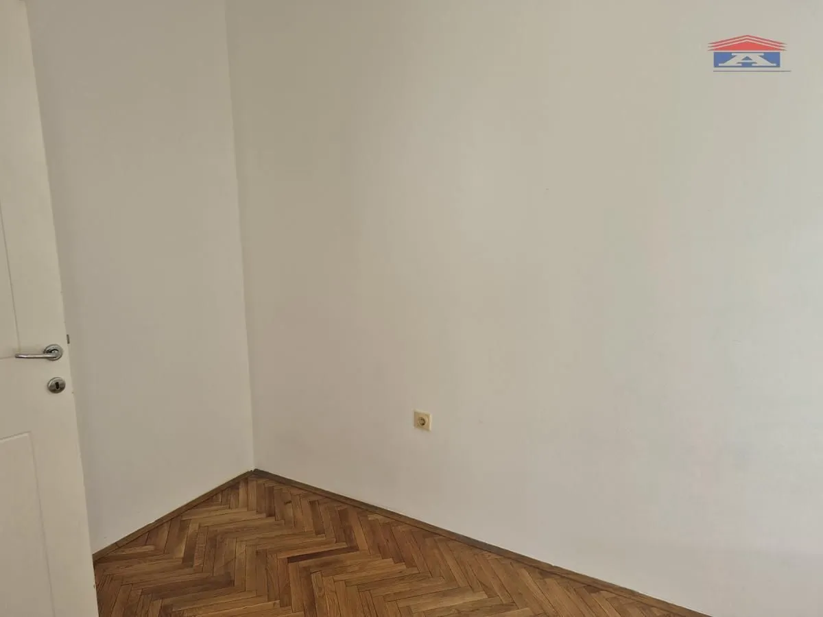 Prazna soba sa parketom i belim zidovima.