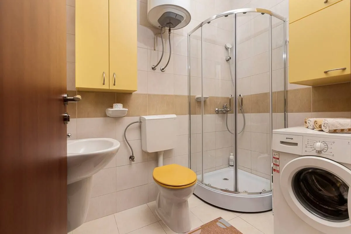 Bathroom equipped with a shower cabin, washbasin, toilet, and washing machine.