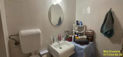 Manje kupatilo sa umivaonikom, ogledalom i WC šoljom obloženo svetlim pločicama. - image 12