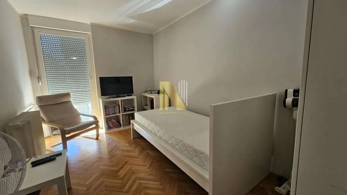 Manja spavaća soba sa krevetom, foteljom i televizorom.