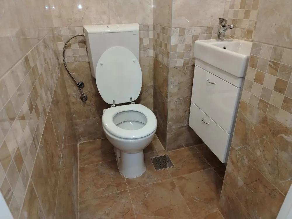 Manje kupatilo obloženo keramičkim pločicama sa WC šoljom i umivaonikom.