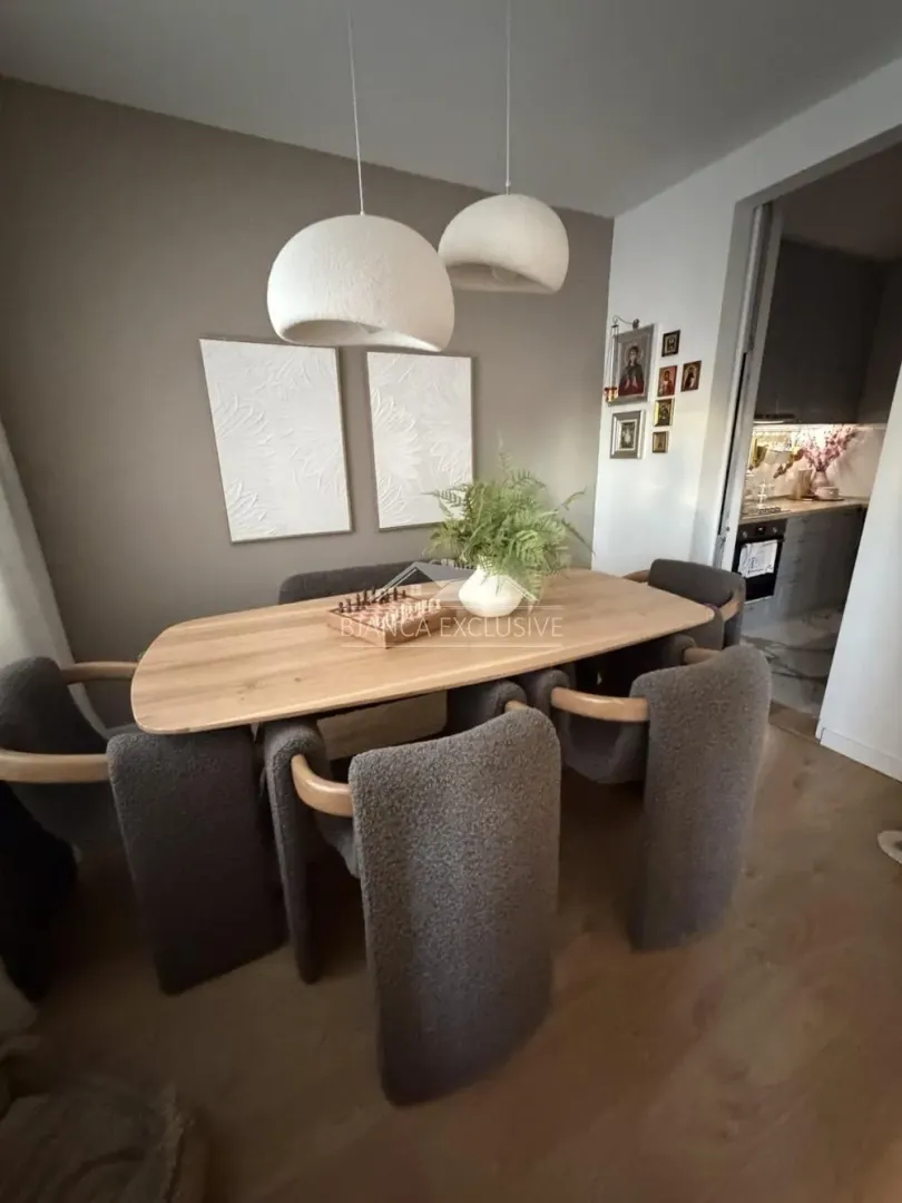 Trpezarija sa drvenim stolom, sivim stolicama i modernim visilicama.