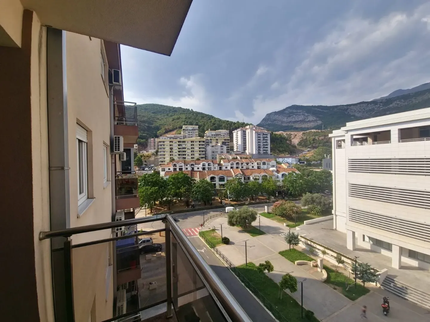 View from the terrace overlooking surrounding buildings, street, and hills in the background.