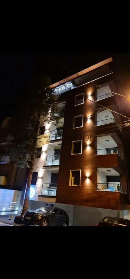 Pogled noću na osvetljenu fasadu stambene zgrade sa terasama.