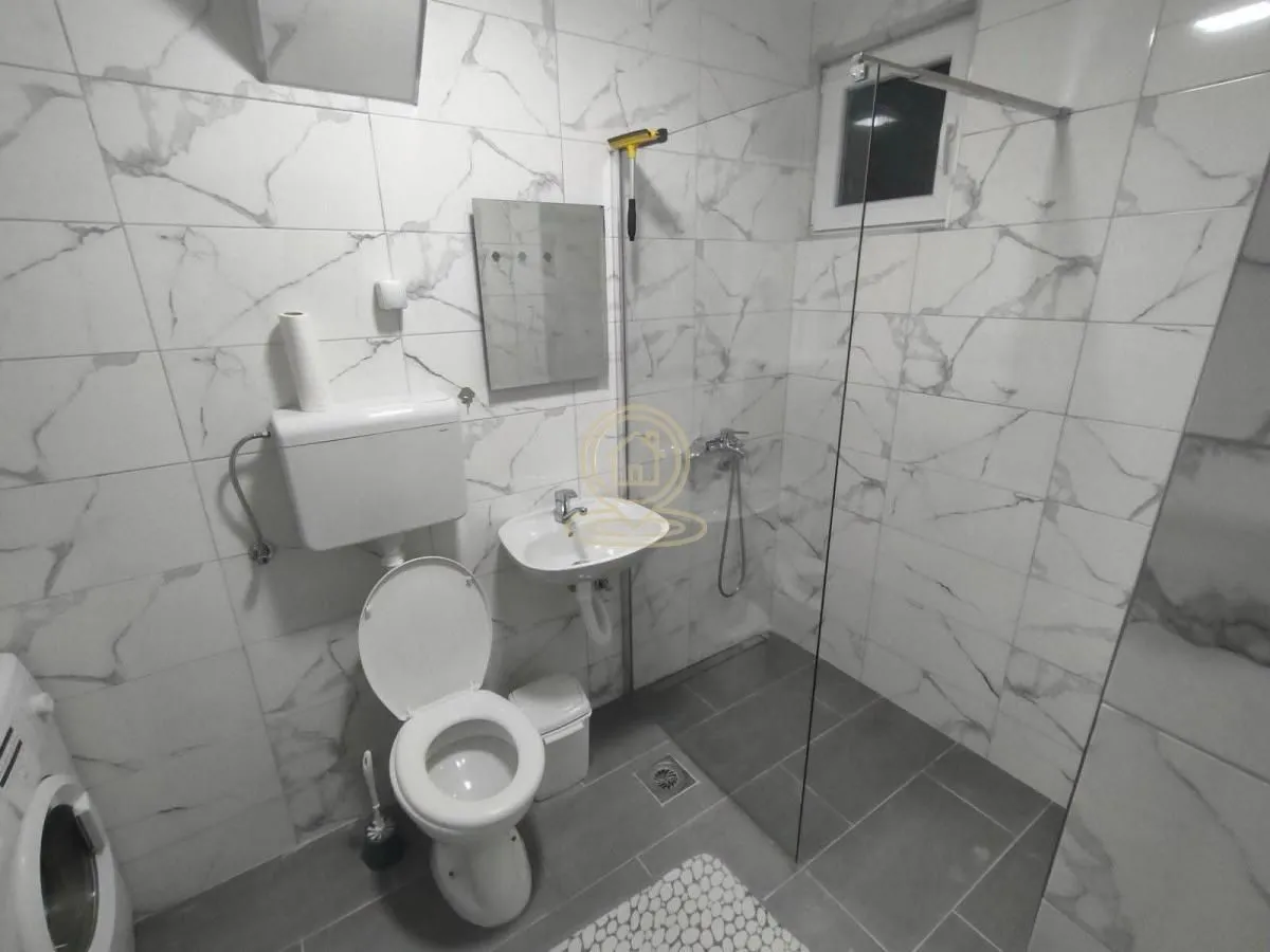 Manje kupatilo obloženo keramičkim pločicama sa tuš kabinom.