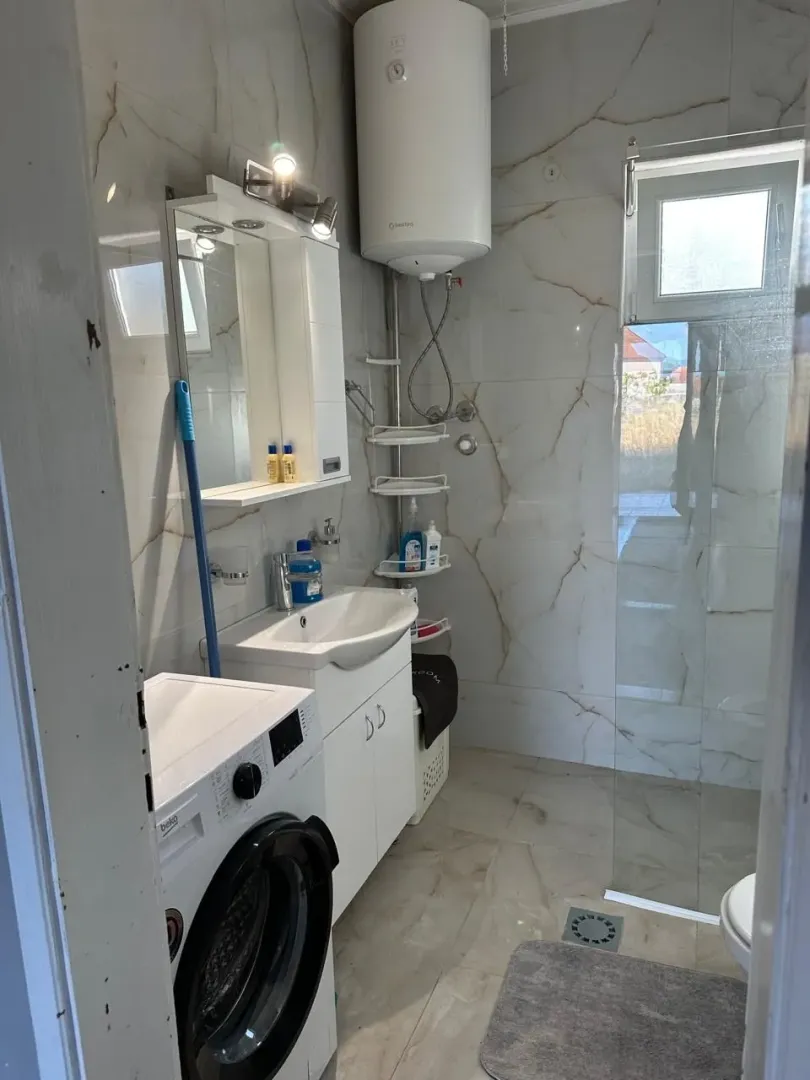 Small bathroom with a sink, shower cabin, water heater, and washing machine.