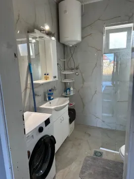 Small bathroom with a sink, shower cabin, water heater, and washing machine. - image 7