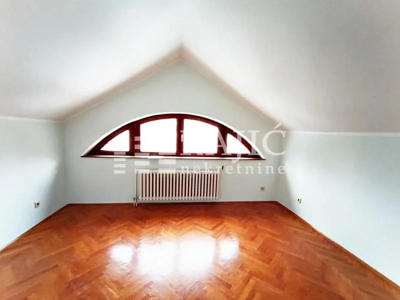 Empty attic room with wooden flooring and a large arched window.