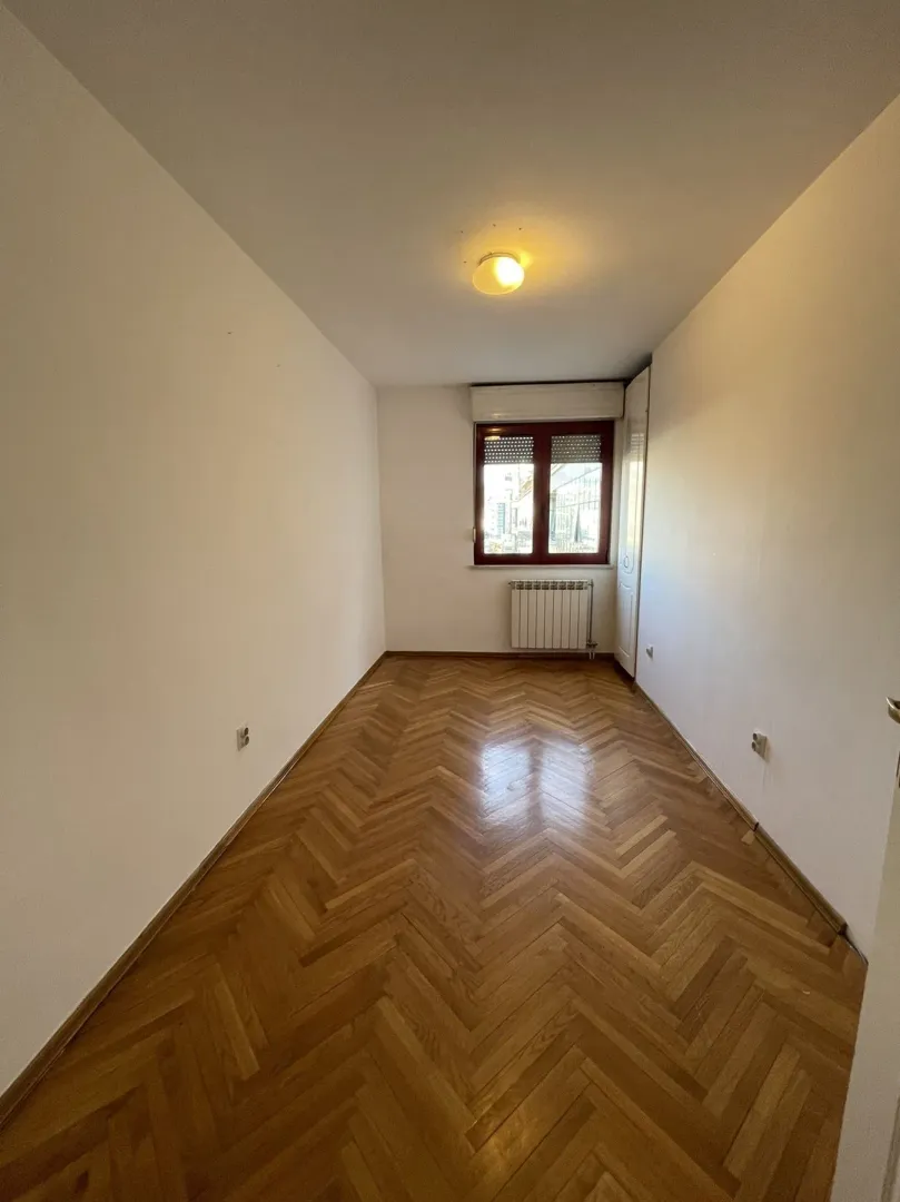 An empty room with parquet flooring and a window.
